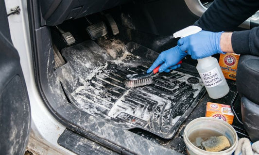 Scrubbing salt stains from rubber car mat with baking soda and cleaning solution